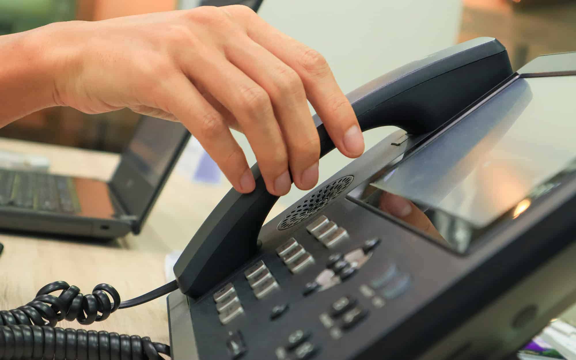 Close-up of someone's hand reaching for an IP phone on a work desk