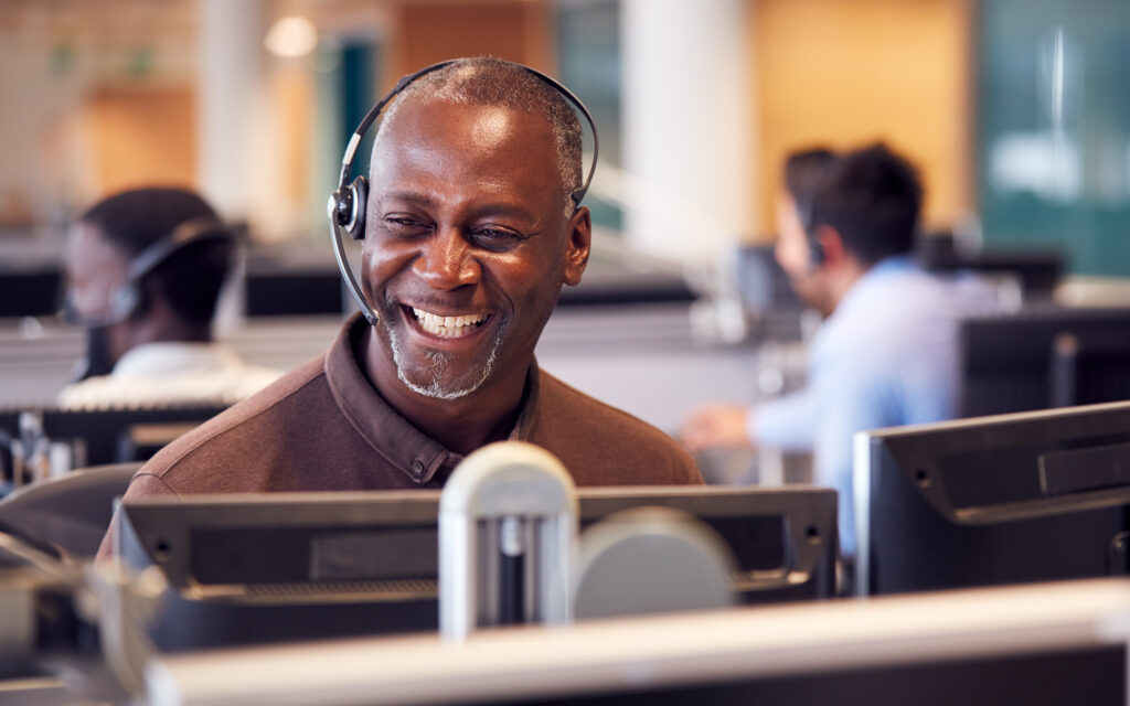 Mature Businessman Wearing Telephone Headset Talking To Caller In Customer Services Department