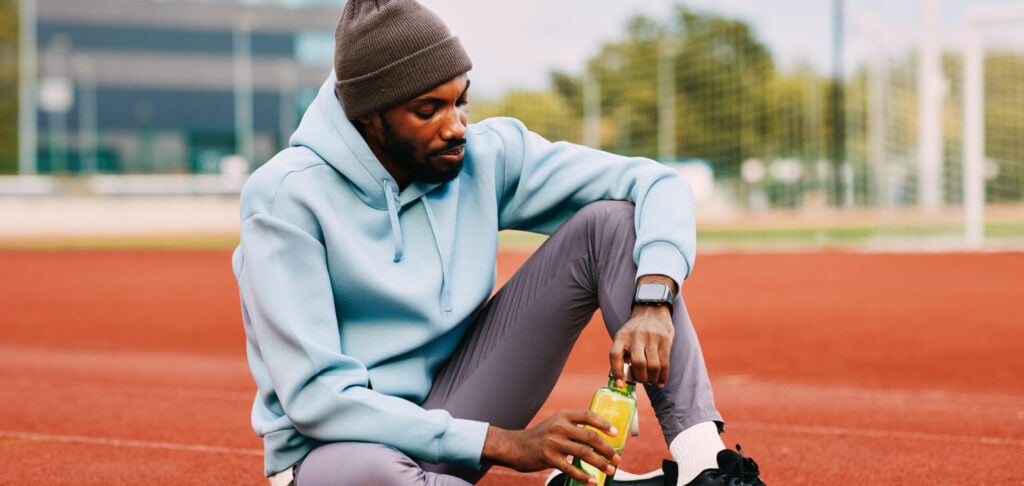 man sitting on a track taking a drink and supplements after a workout