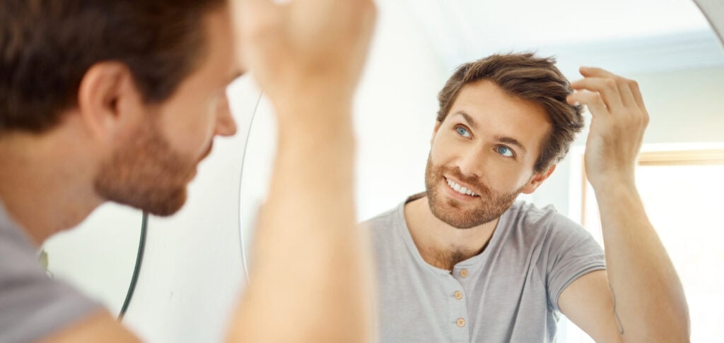 Bathroom, mirror reflection and happy man with hair care routine for maintenance, beauty process or hygiene cleaning treatment. Smile, morning and home person style locks for clean shampoo hairstyle.
